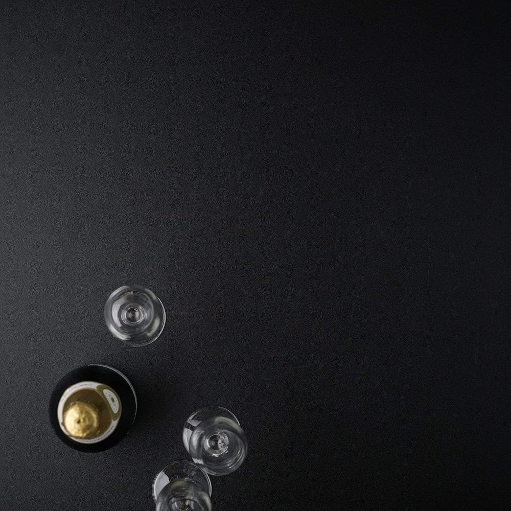 A gold-foiled champagne bottle and three empty wine glasses rest on a Bengal Black Restaurant Table Top - 25mm, viewed from above with ample negative space on the right.
