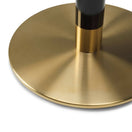Switch Close-up of the Cava Round Black and Gold Table Base - Large, featuring a cylindrical black and gold column attached to a large, round brushed brass base that casts soft reflections on its metallic surface. 2 image