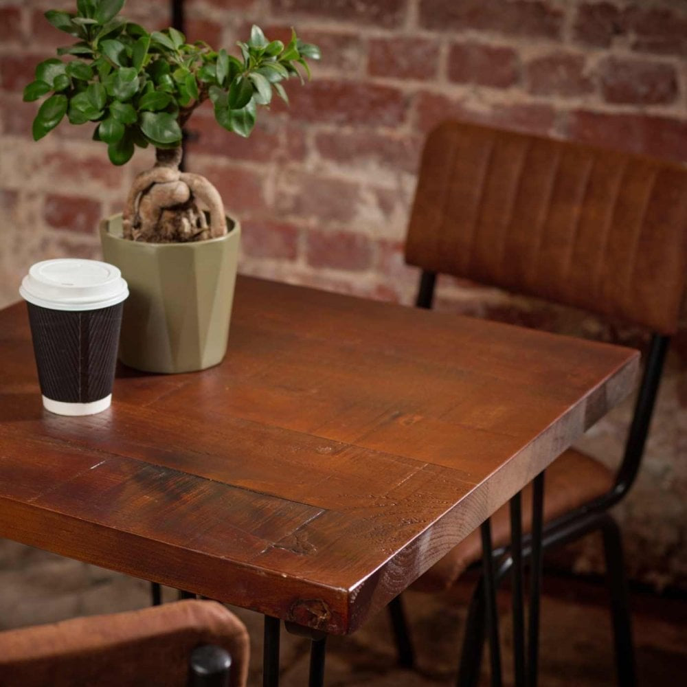 A Barrel Pine Solid Wood Table Top - 34mm with a potted plant and takeaway coffee cup sits beside two brown chairs, all set against a charming brick wall.