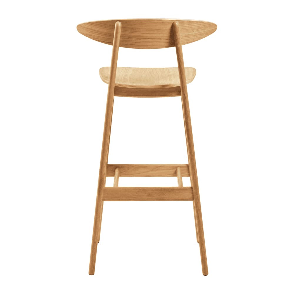 The Carcher Oak Bar Stool features a modern design with a curved backrest and angled legs, crafted from light oak. Its minimalistic style makes it ideal for contemporary interiors and looks stunning when viewed from behind.