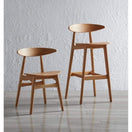 Switch The Carcher Oak Bar Stool, with its minimalist design and curved backrest, crafted from solid oak, stands on a light wooden floor and enhances the contemporary interior against a textured white wall. 2 image
