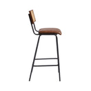 Switch Side view of the Savanna Bar Stool with a black metal frame, brown genuine leather seat, and rectangular natural cane backrest. Slender legs with footrest connect the front and back legs for added convenience. 3 image