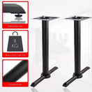 Switch The Antonio Twin Pedestal Cast Iron Table Base is displayed in black with a T-shaped design. Inset images show adjustable feet, an 8 kg heavy-duty build, and a smooth finish. The backdrop is a bright room with large windows. 1 image