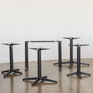 Switch Four Trail Black Self Levelling Table Bases - Rectangle Single Pedestal by NOROCK stand upright on a polished concrete floor against a plain white wall. Designed for indoor and outdoor use, these bases have no tabletops attached. 3 image