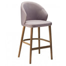 Switch The Serene Raw Barstool Frame features a curved, upholstered lavender seat and backrest, supported by four solid wood legs with a connecting footrest. 2 image