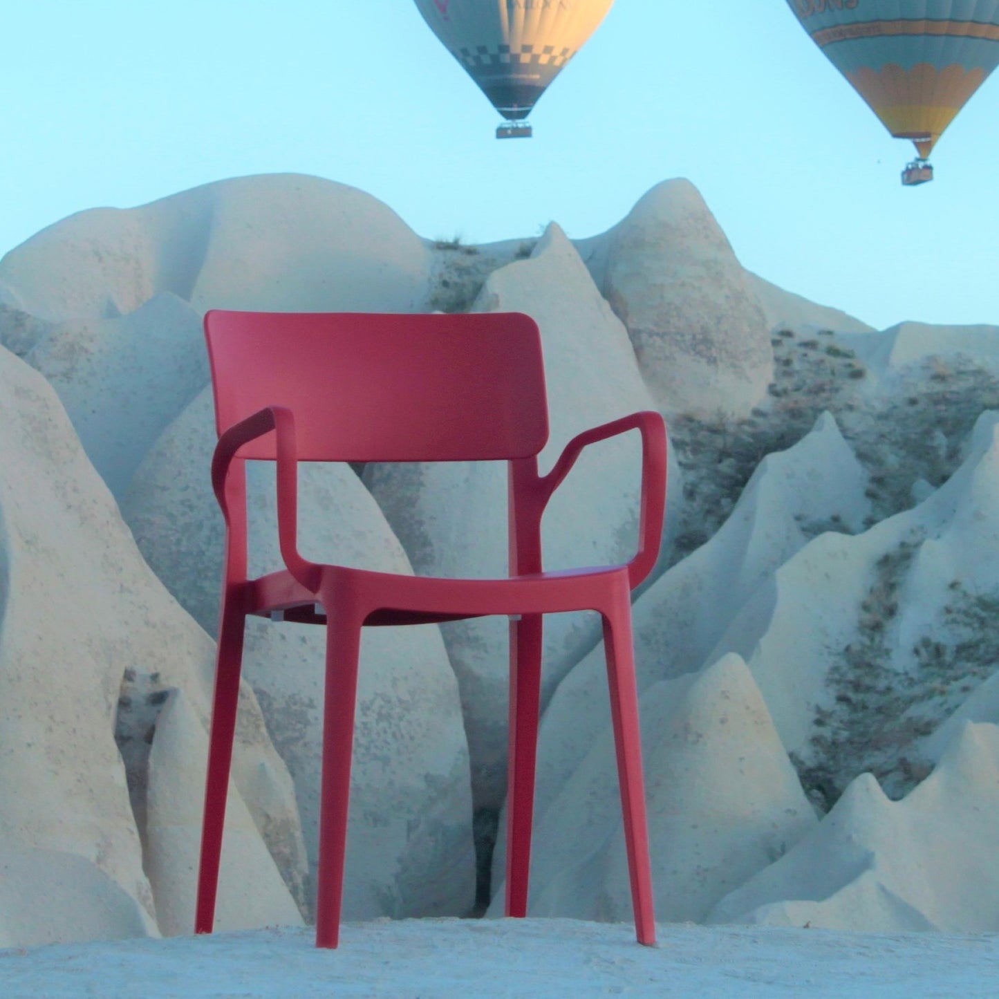 A Vivo Stacking Outdoor Armchair rests on light rocky terrain with striking formations, while hot air balloons drift above—creating a surreal scene that showcases this modern chair’s versatility for stylish indoor and outdoor use.