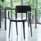 Switch The Vivo Stacking Outdoor Armchair in modern black, featuring armrests, sits on a polished concrete floor in a bright room with large windows, a table, and green plants—a perfect blend of indoor-outdoor chair style. 2 image